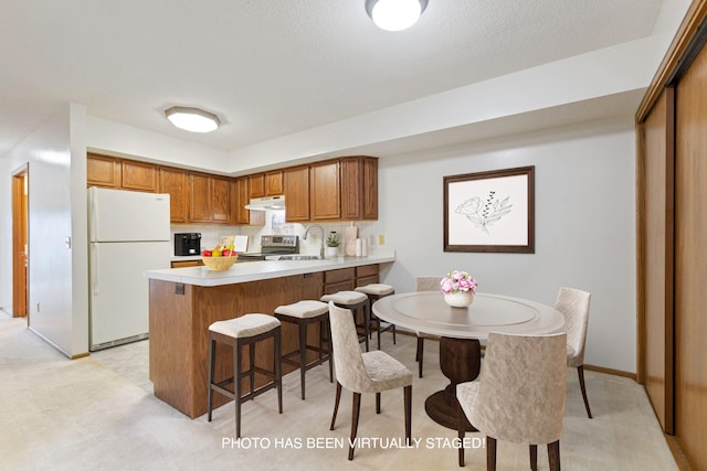 kitchen featuring under cabinet range hood, light countertops, a peninsula, stainless steel range with electric cooktop, and freestanding refrigerator