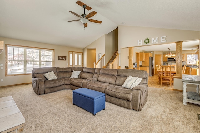 living room featuring stairway, light carpet, a healthy amount of sunlight, and ceiling fan with notable chandelier