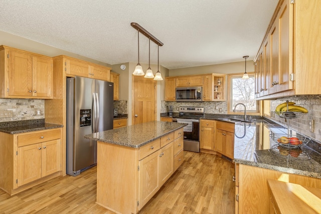 kitchen with a kitchen island, dark stone counters, light wood-type flooring, stainless steel appliances, and a sink