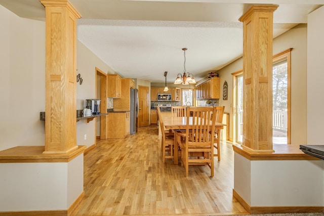 dining space featuring a chandelier, light wood-style flooring, and decorative columns