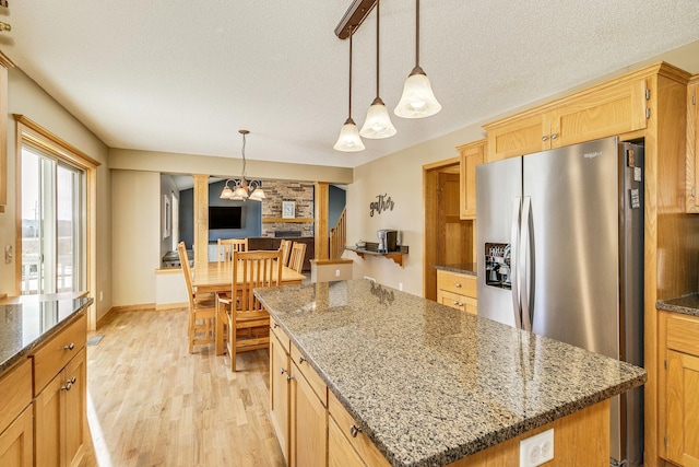 kitchen with light wood-type flooring, a textured ceiling, a center island, dark stone counters, and stainless steel fridge