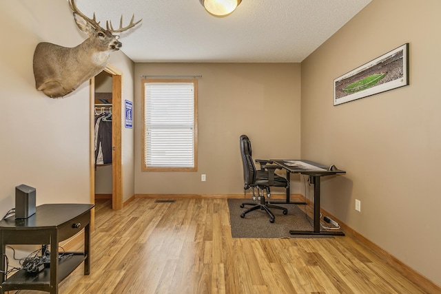 office featuring light wood-style flooring, a textured ceiling, and baseboards