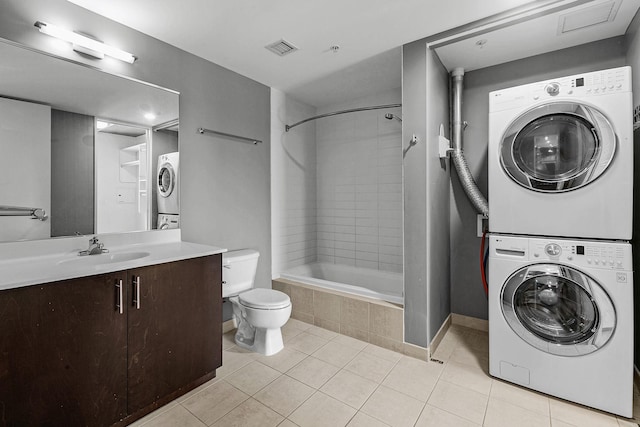 full bathroom featuring visible vents, tiled shower / bath, toilet, stacked washing maching and dryer, and tile patterned flooring