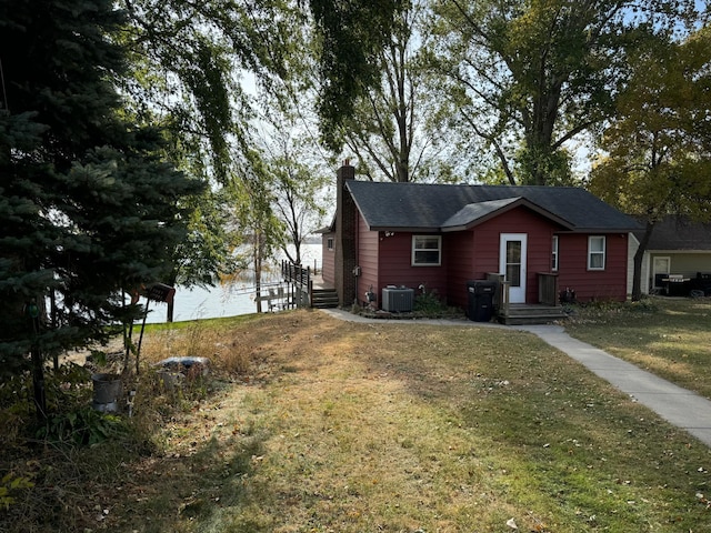 exterior space with central AC unit, a chimney, a yard, and a water view