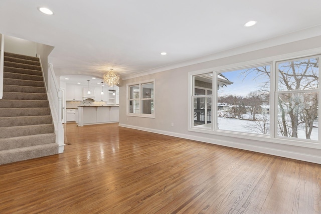 unfurnished living room featuring light wood-style flooring, recessed lighting, stairway, an inviting chandelier, and baseboards