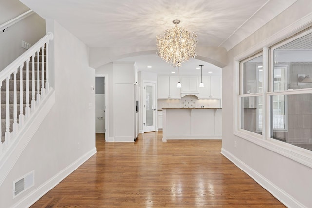 unfurnished living room with visible vents, stairway, baseboards, and wood finished floors