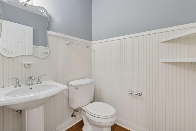 bathroom featuring wood finished floors, wainscoting, toilet, and a sink