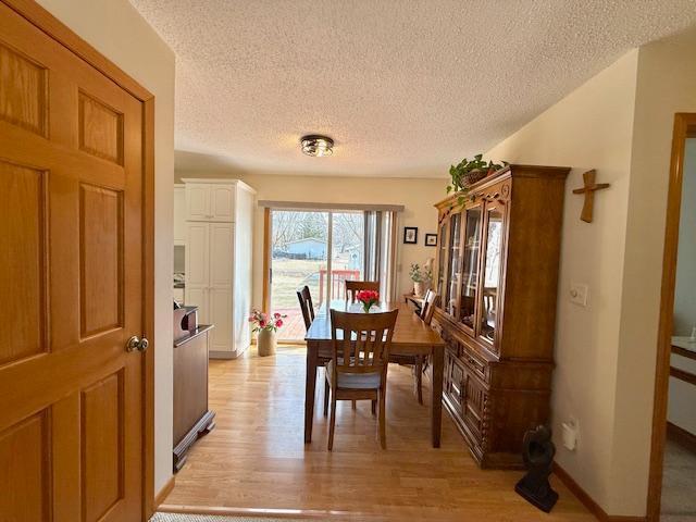 dining room with baseboards, light wood-style floors, and a textured ceiling