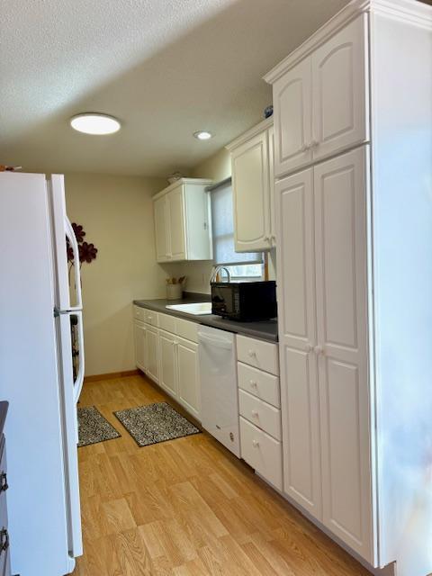 kitchen with white appliances, light wood finished floors, a textured ceiling, white cabinetry, and dark countertops