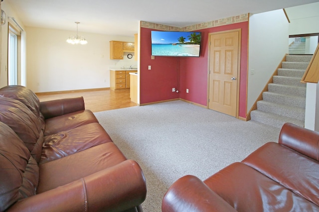 living room with stairway, baseboards, light wood finished floors, a notable chandelier, and light colored carpet