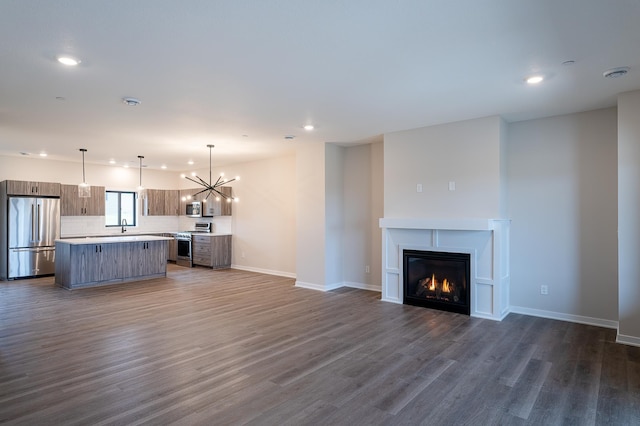 unfurnished living room with baseboards, recessed lighting, dark wood-type flooring, a glass covered fireplace, and a notable chandelier