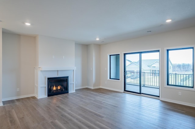 unfurnished living room featuring a glass covered fireplace, recessed lighting, wood finished floors, and baseboards