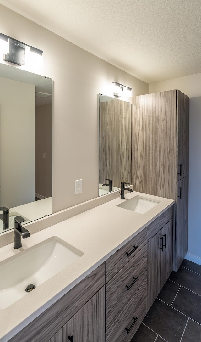 bathroom with a sink, a textured ceiling, double vanity, and tile patterned flooring