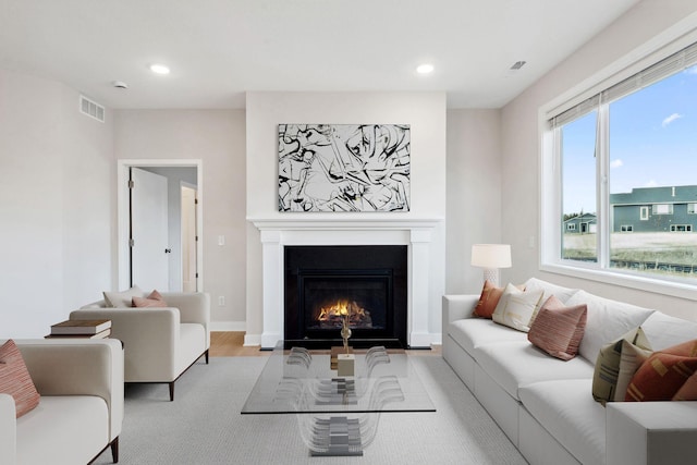 living room featuring recessed lighting, visible vents, wood finished floors, and a warm lit fireplace