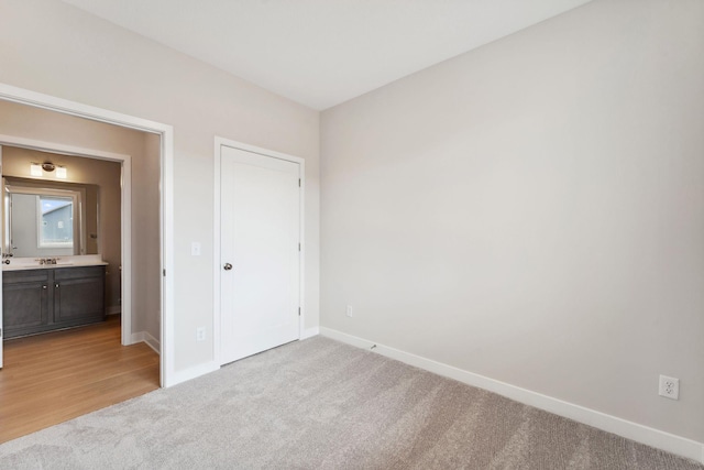 unfurnished bedroom with baseboards, light carpet, and a sink