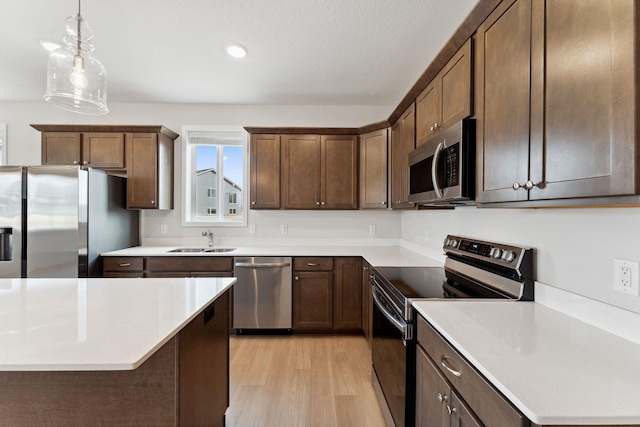 kitchen with stainless steel appliances, light wood-style floors, light countertops, a sink, and pendant lighting