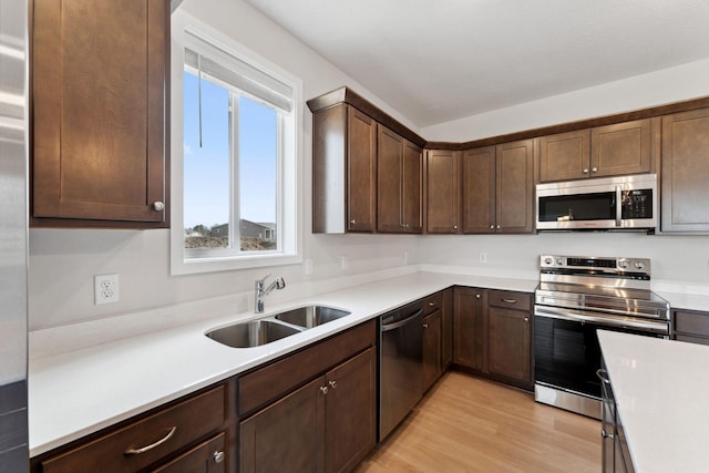 kitchen with dark brown cabinetry, stainless steel appliances, light countertops, light wood finished floors, and a sink