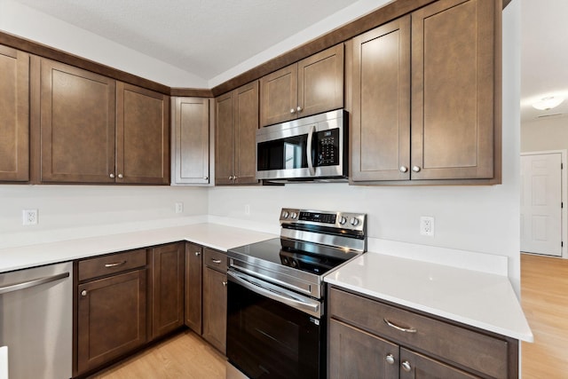 kitchen featuring light wood finished floors, dark brown cabinets, appliances with stainless steel finishes, and light countertops