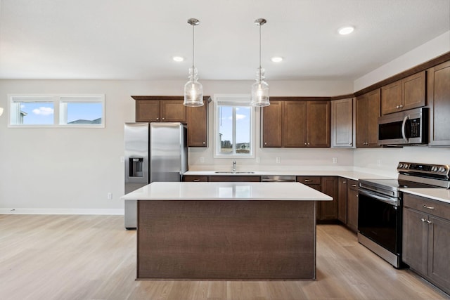 kitchen featuring a sink, light wood-style floors, a center island, dark brown cabinetry, and appliances with stainless steel finishes