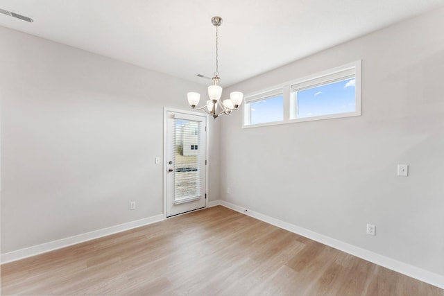 empty room with visible vents, baseboards, a chandelier, and light wood-style floors