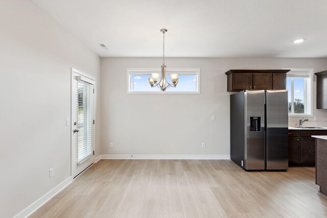 kitchen with a sink, a chandelier, light wood-style floors, dark brown cabinetry, and stainless steel fridge with ice dispenser