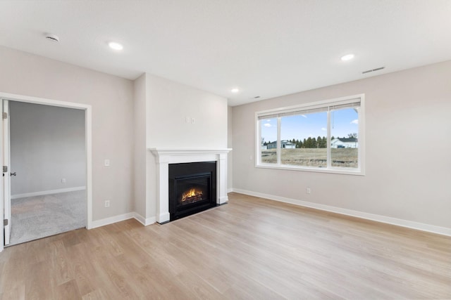 unfurnished living room with recessed lighting, light wood-style floors, baseboards, visible vents, and a fireplace with flush hearth