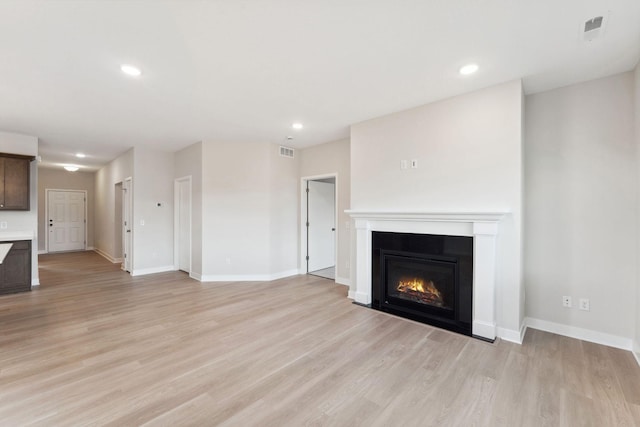 unfurnished living room with a glass covered fireplace, visible vents, light wood finished floors, and baseboards