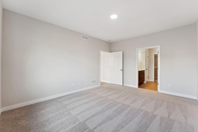 unfurnished bedroom featuring baseboards, visible vents, light carpet, and ensuite bathroom