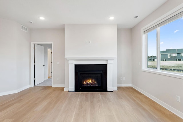 unfurnished living room with visible vents, a lit fireplace, baseboards, recessed lighting, and wood finished floors