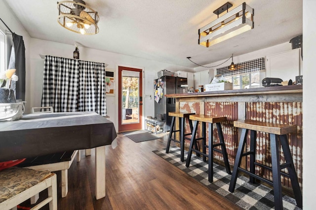 dining space with a bar, dark wood-style floors, and a textured ceiling