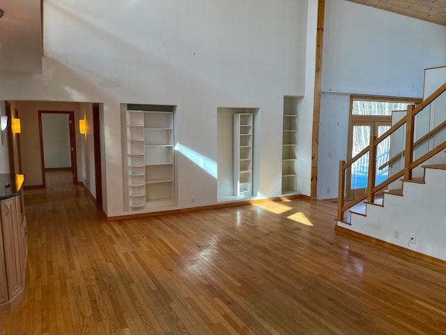 unfurnished living room with light wood-type flooring, baseboards, a towering ceiling, and stairs