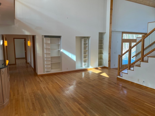 unfurnished living room with built in features, stairs, a high ceiling, and hardwood / wood-style floors