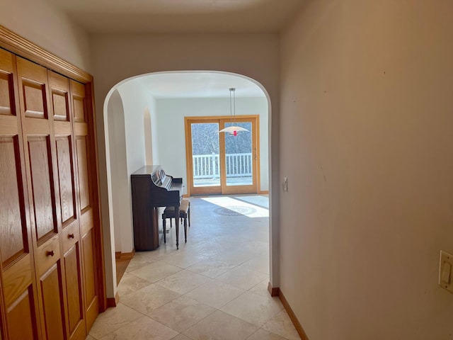 hall featuring arched walkways, light tile patterned floors, and baseboards