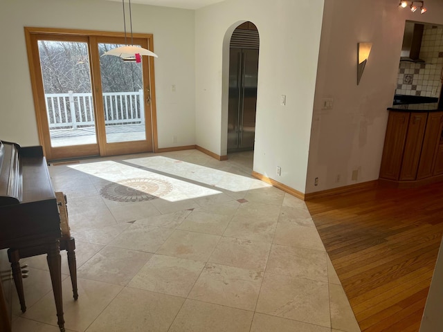 unfurnished living room with arched walkways, light wood-style floors, and baseboards