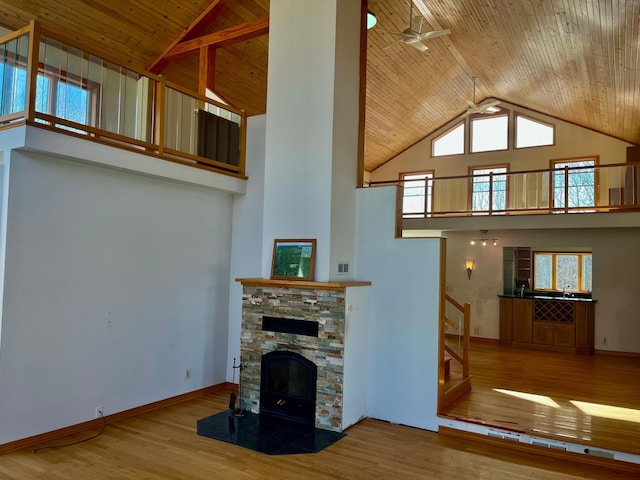 unfurnished living room with a stone fireplace, wood ceiling, wood finished floors, and high vaulted ceiling