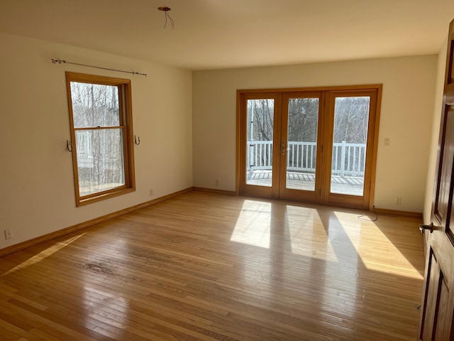 empty room with a wealth of natural light, french doors, baseboards, and light wood finished floors