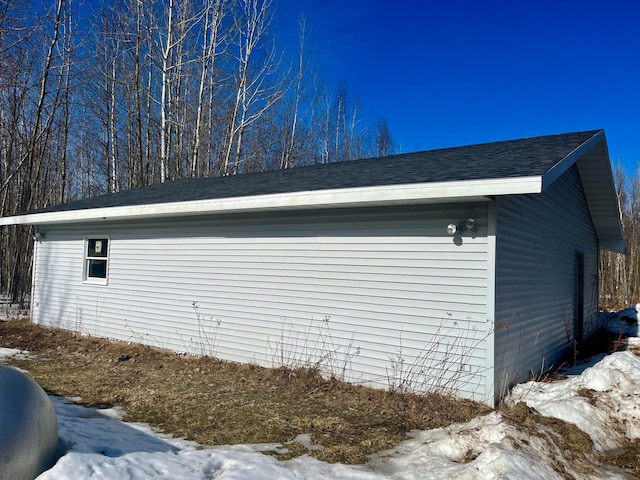 snow covered property with an outdoor structure and a shingled roof