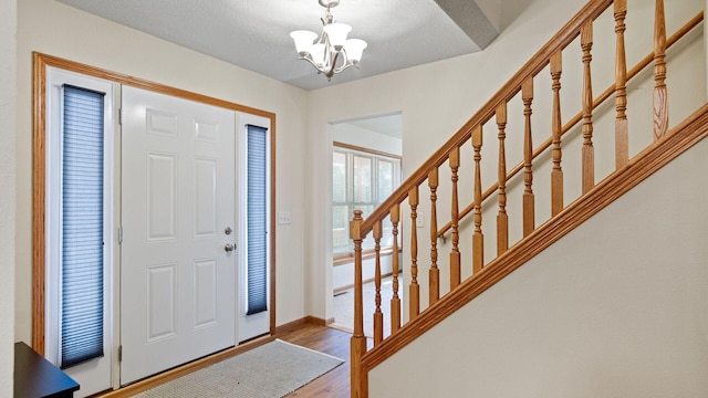 entryway featuring stairway, wood finished floors, baseboards, and a chandelier