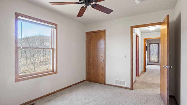 unfurnished bedroom featuring ceiling fan, light colored carpet, visible vents, and baseboards