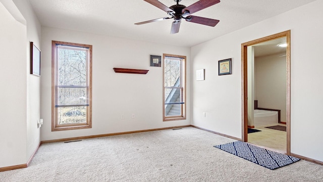 spare room with carpet flooring, ceiling fan, baseboards, and visible vents