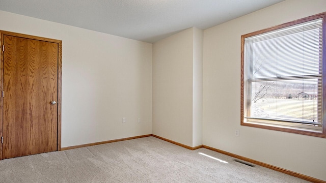 empty room with visible vents, light colored carpet, and baseboards