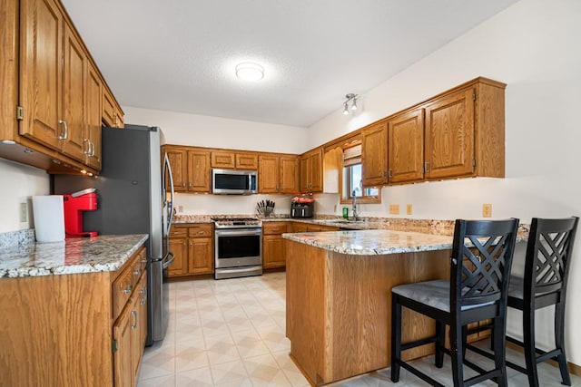 kitchen with a sink, a kitchen breakfast bar, stainless steel appliances, a peninsula, and brown cabinetry