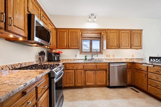 kitchen featuring a sink, brown cabinetry, light stone countertops, and stainless steel appliances