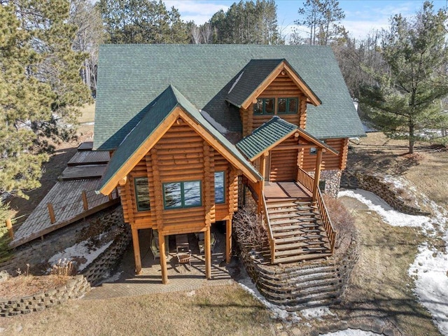 cabin with log siding, stairway, and roof with shingles