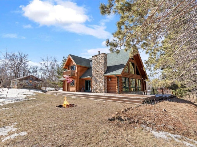 view of property exterior with a fire pit, roof with shingles, log siding, a chimney, and a balcony