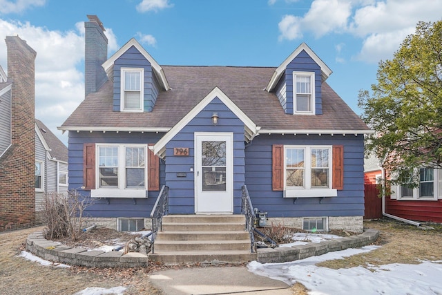 cape cod home with entry steps, roof with shingles, and a chimney