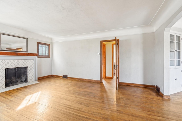 unfurnished living room with visible vents, wood finished floors, baseboards, and a tile fireplace