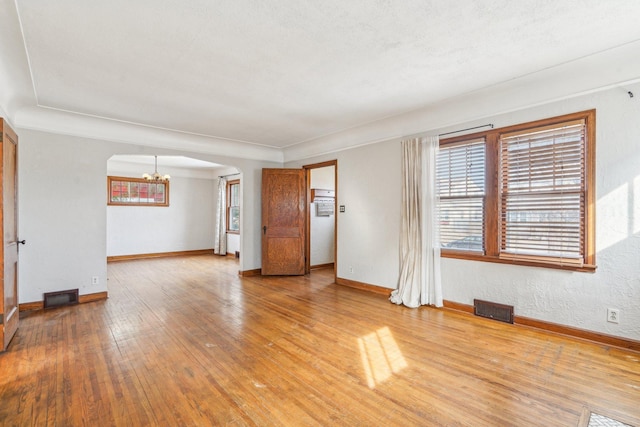 unfurnished living room with arched walkways, visible vents, light wood finished floors, and a chandelier