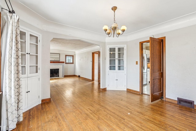 unfurnished dining area with visible vents, light wood-style flooring, a fireplace, arched walkways, and a notable chandelier