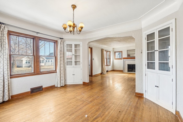 unfurnished dining area featuring baseboards, visible vents, an inviting chandelier, arched walkways, and light wood-type flooring